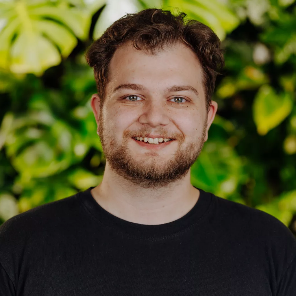 Lukas Fischer, Projektleiter bei Vertiko, steht vor einer grünen Pflanzenwand