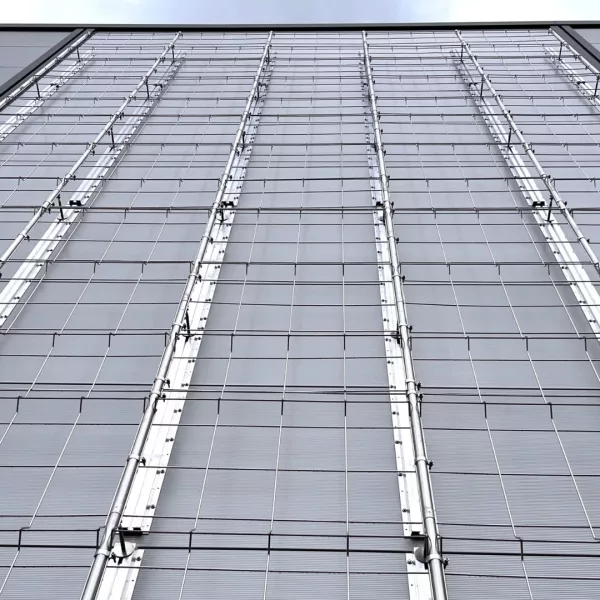 Metallisches Rankgittersystem mit vertikalen Halterungen an einer grauen Gebäudefassade.