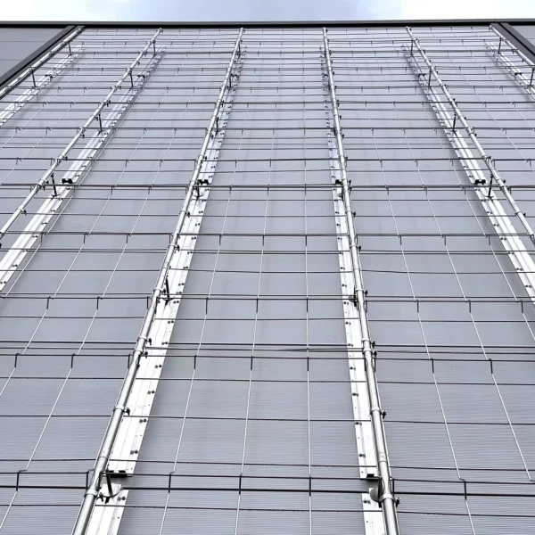 Metallisches Rankgittersystem mit vertikalen Halterungen an einer grauen Gebäudefassade.